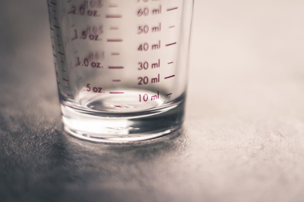 Small glass measuring cup marked in fluid ounces and milliliters, sized for measuring a softener sanitizing dose