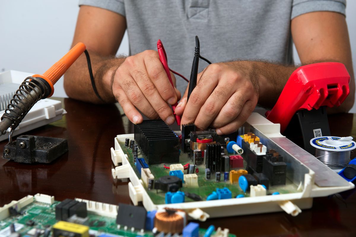 Technician repairing an electronic circuit board with hand tools on a workbench, the kind of control board that generates a water softener error code