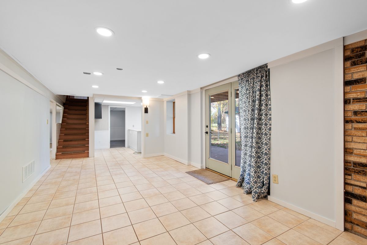 Finished basement with a tile floor, a staircase and glass doors to a walk-out patio, a warm location near where a home's water main typically enters