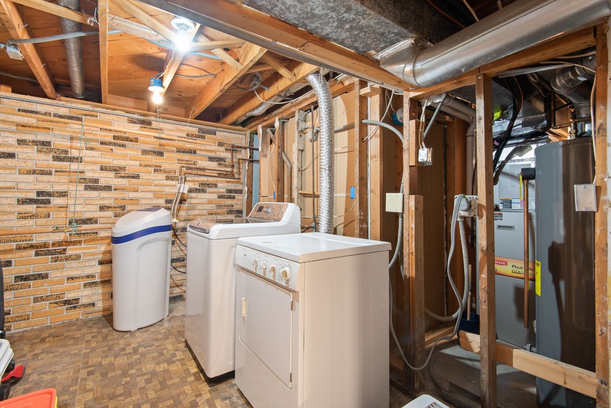 Bright basement laundry area with utility connections, the kind of space where a softener and water heater sit together and share a smell problem