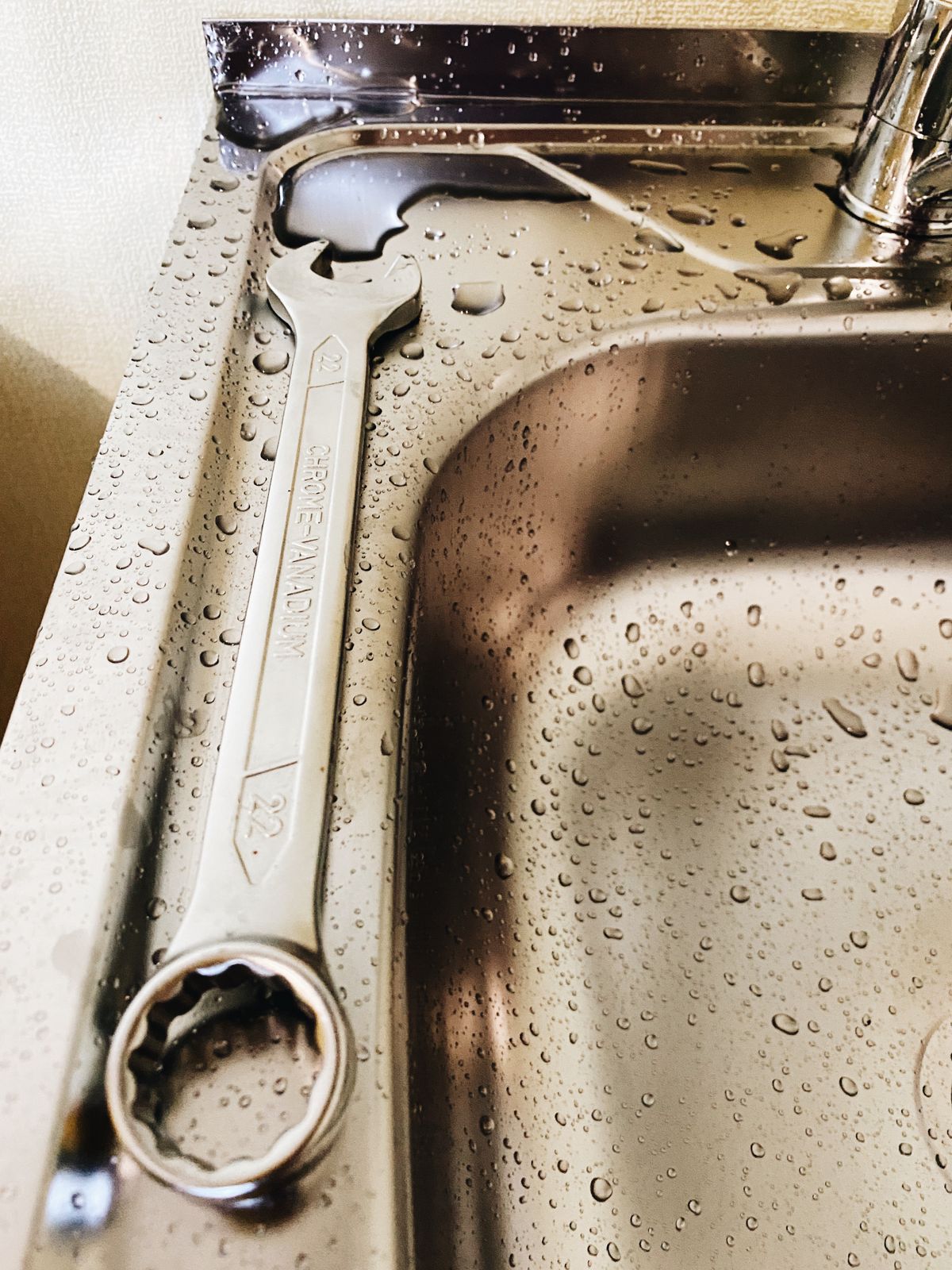 Metal wrench resting on a stainless steel sink beside water droplets during a faucet repair