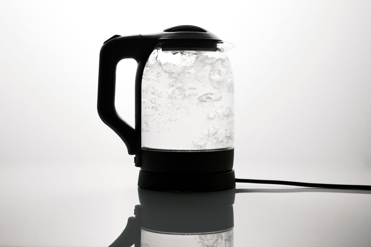 Sleek electric kettle boiling water on a reflective white surface, where limescale in kettle and coffee maker interiors begins