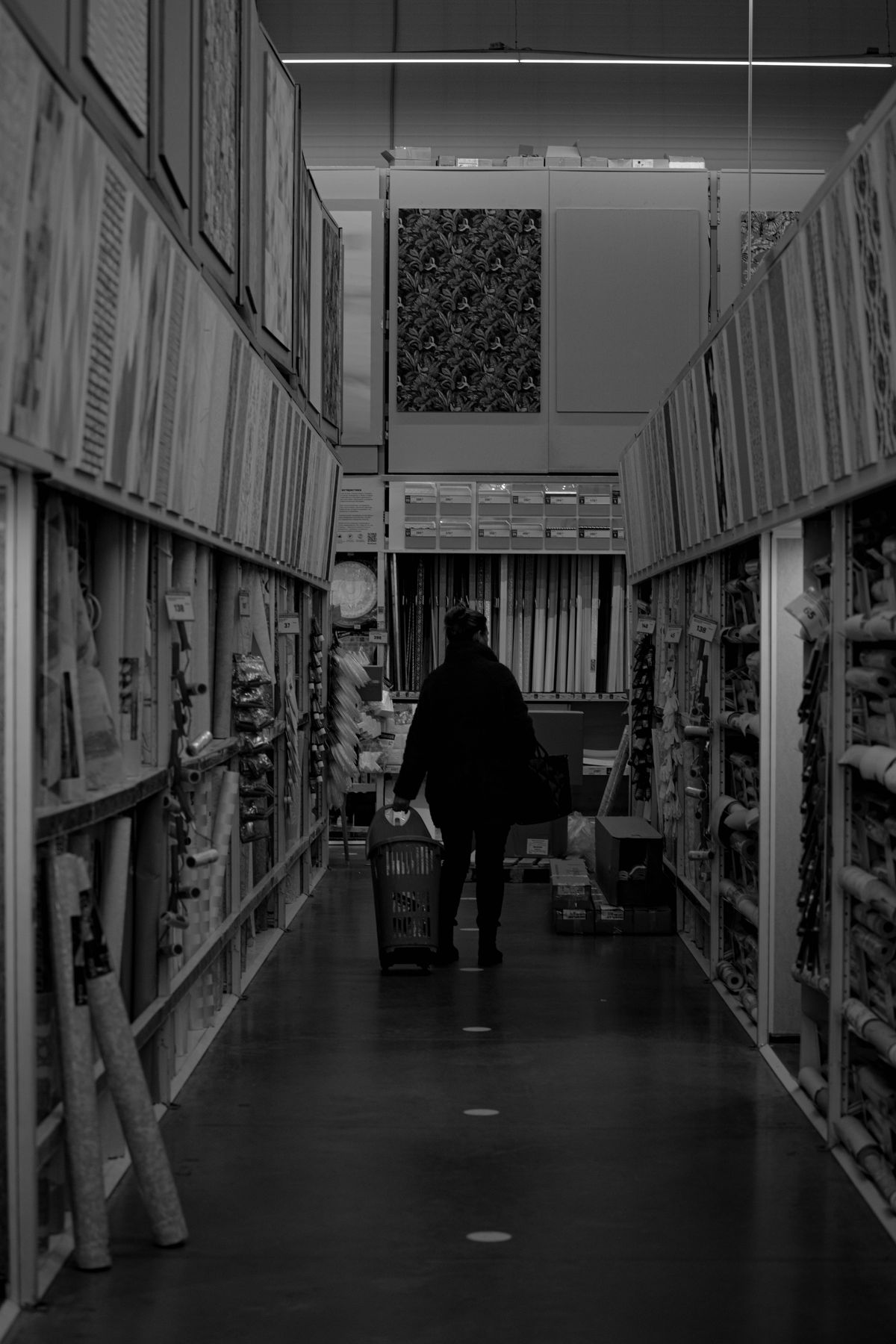 Black and white photo of a shopper walking down a long DIY store aisle, the big-box setting where Home Depot and Lowe's sell water softeners