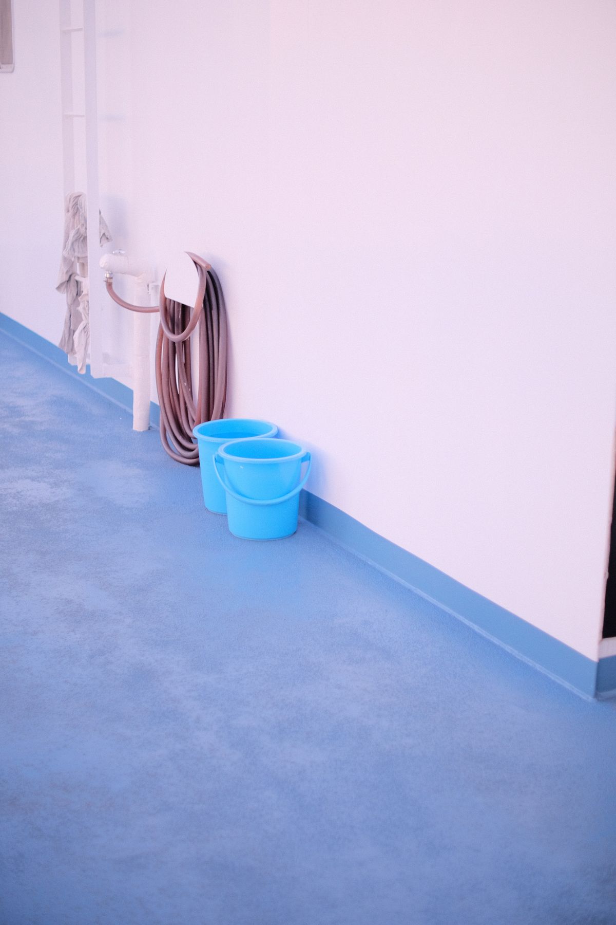 Two blue plastic buckets beside a hose on a wall-mounted spigot, the kit for a timed bucket test of well pump flow rate