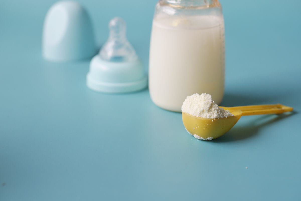 Scoop of infant formula powder beside a baby bottle of mixed formula, prepared with unsoftened water rather than softened water