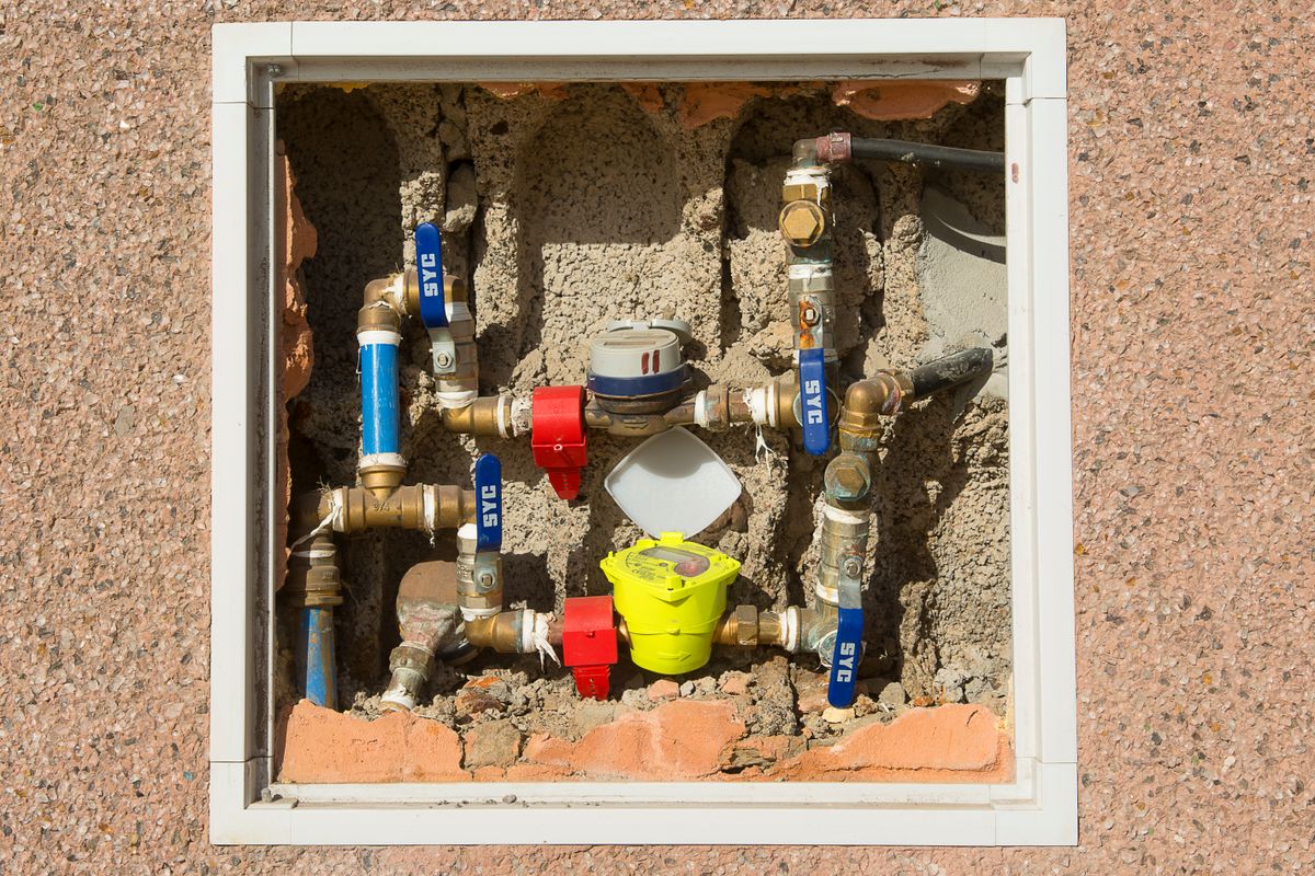 Domestic water meter and pipework set into a concrete wall, the counter that tells you whether a demand-initiated softener is still measuring flow