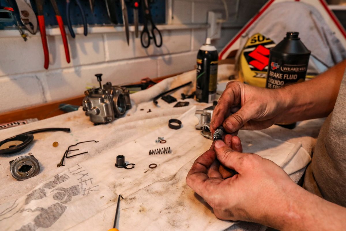 Hands working on a disassembled mechanical assembly with tools on a workbench, the same careful strip-down used to clean and reseal a water softener control valve