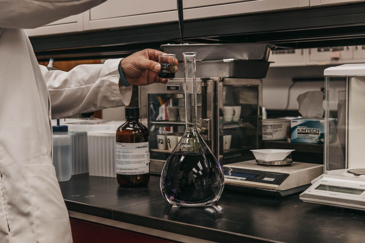Hand holding a small glass beaker of clear liquid, representing the careful measured dose that should stop once cleaning no longer recovers resin capacity