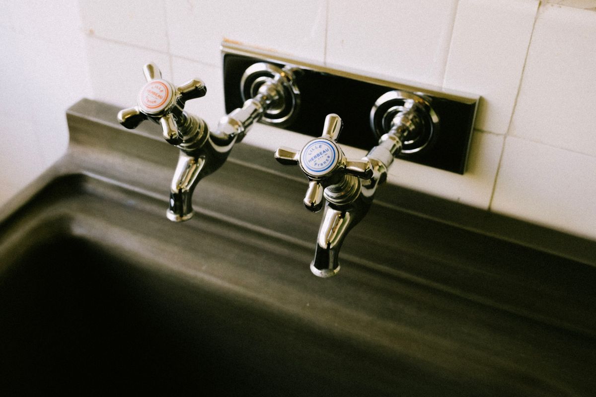 Chrome kitchen sink faucets with hot and cold handles showing white spots on faucets from mineral deposits