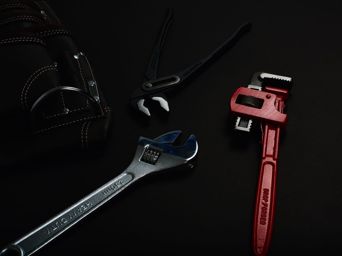 Assorted wrenches and pliers laid out on a dark surface, the basic hand tools needed to open brine line fittings and remove a softener injector cap