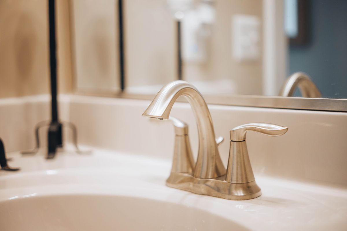 Brushed brass bathroom faucet over a white basin, the kind of cold-water tap used to sample hardness with the softener in bypass and again in service