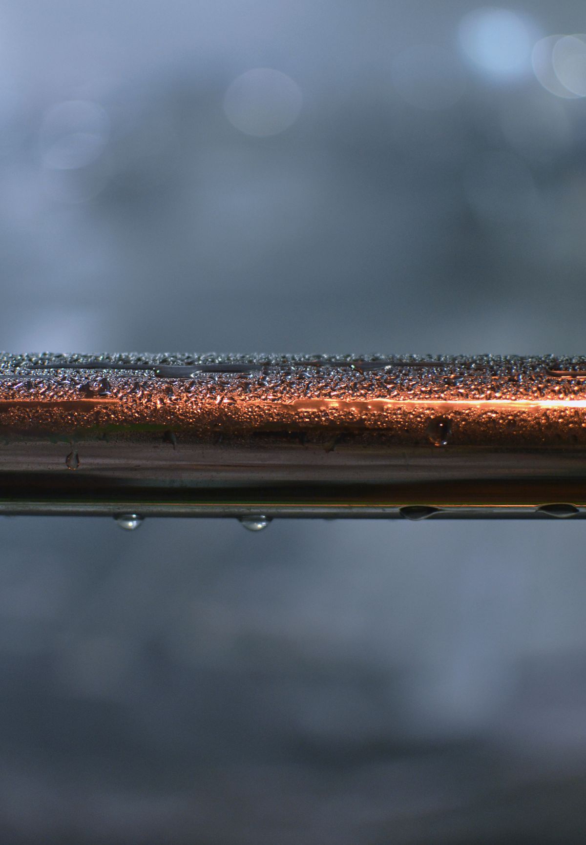 Close-up of a copper water supply pipe beaded with water droplets along its length