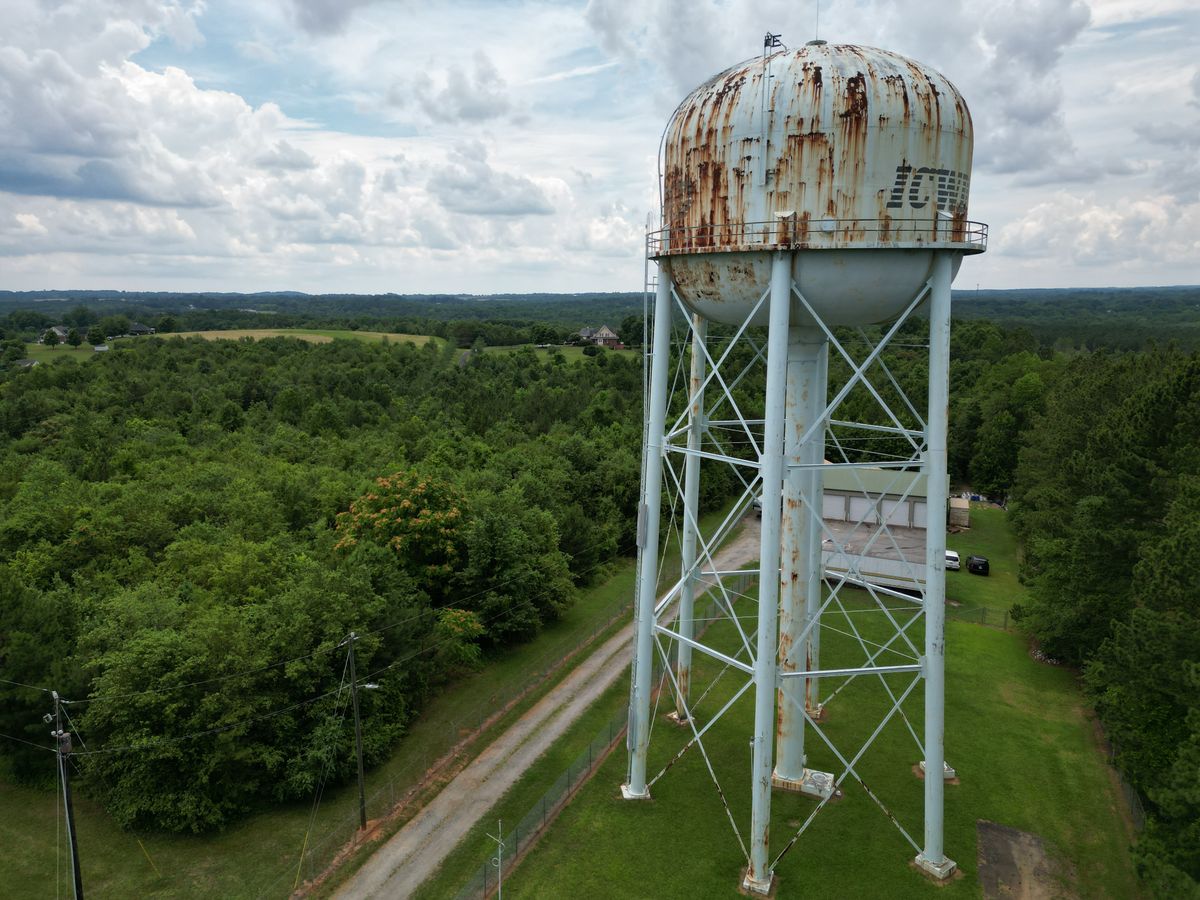 Aerial view of an elevated municipal water storage tank on steel legs among trees, where chloraminated water can sit for days in the distribution system