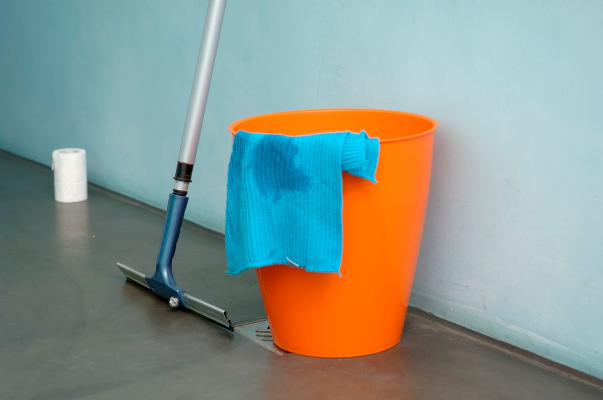 Orange bucket with a mop and cleaning cloth standing ready indoors, the basic kit a brine tank cleanout needs