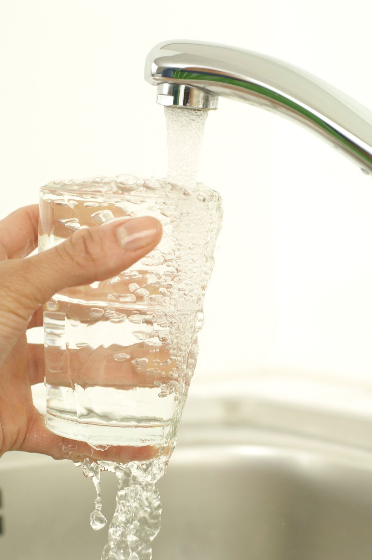 Hand holding a glass being filled with tap water