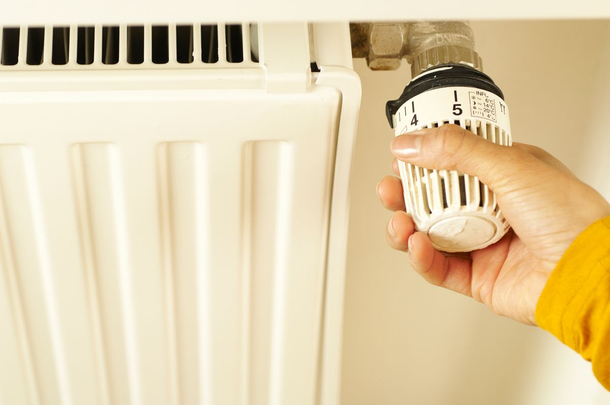 Hand adjusting a radiator thermostat, the kind of temperature control that keeps a garage or utility room housing a water softener above 40°F all winter