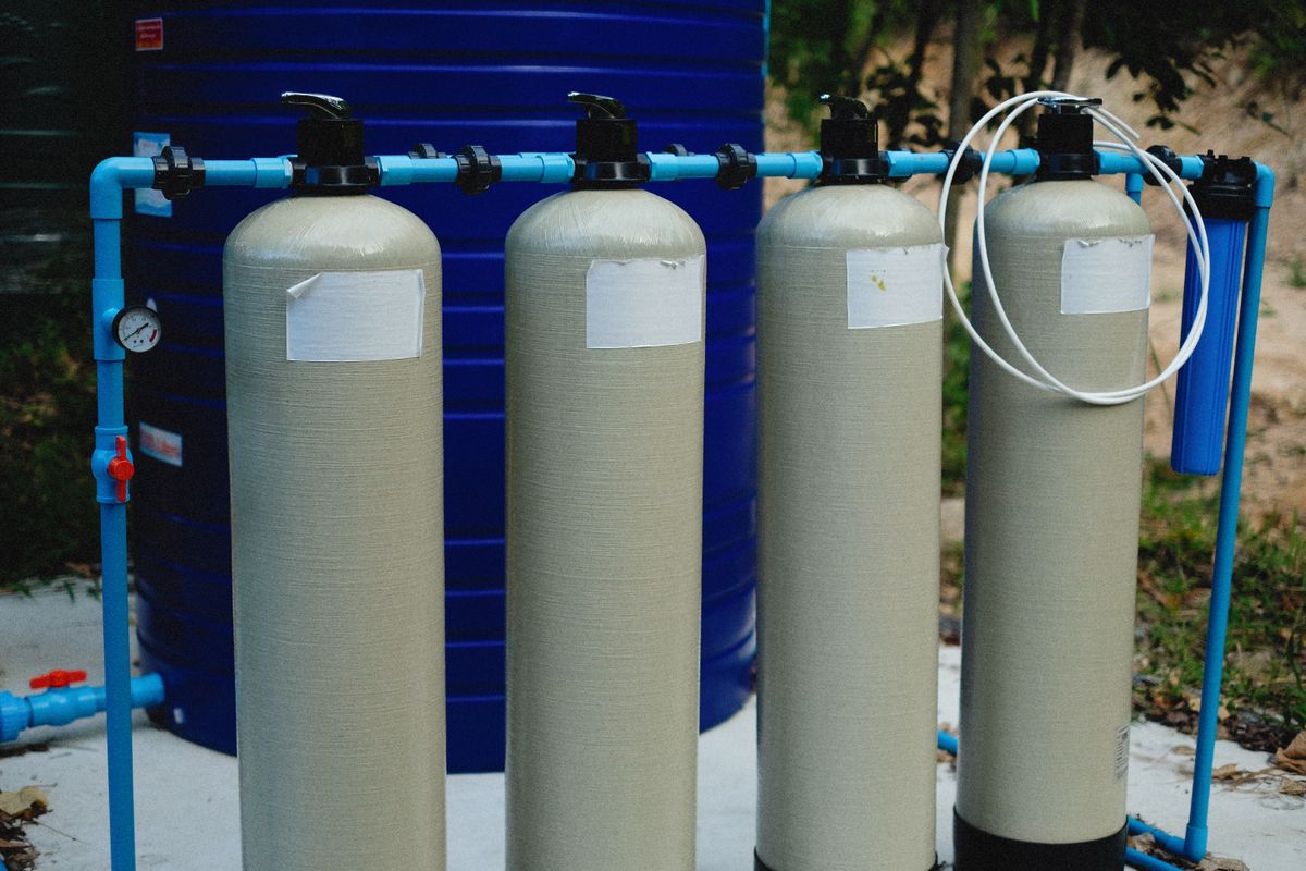 Row of fibreglass water treatment tanks connected by blue piping, the kind of equipment behind the question of whether you need a whole house water softener