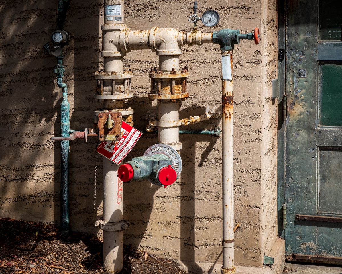 Outdoor plumbing manifold with pressure gauges and valves, the kind of fitting used to draw a raw well water sample