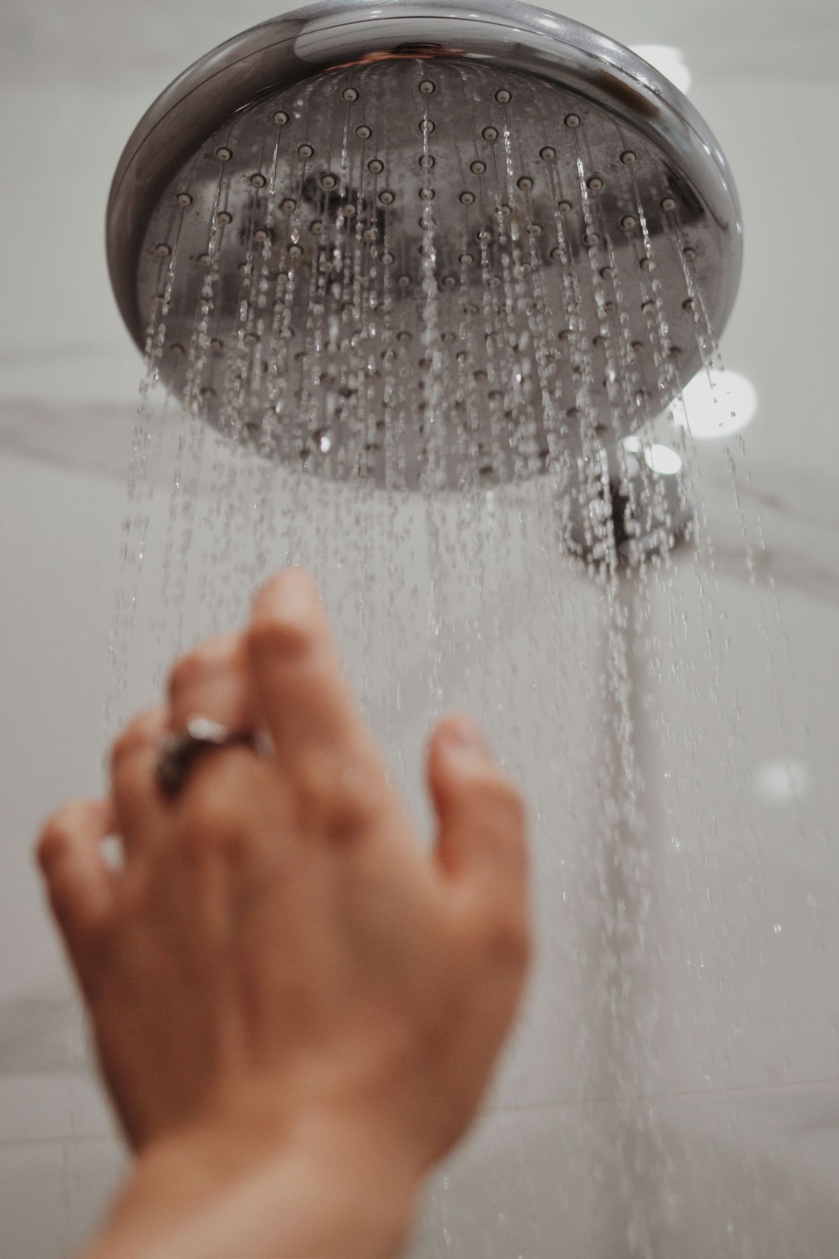 Hand reaching towards a running shower head with water droplets in motion