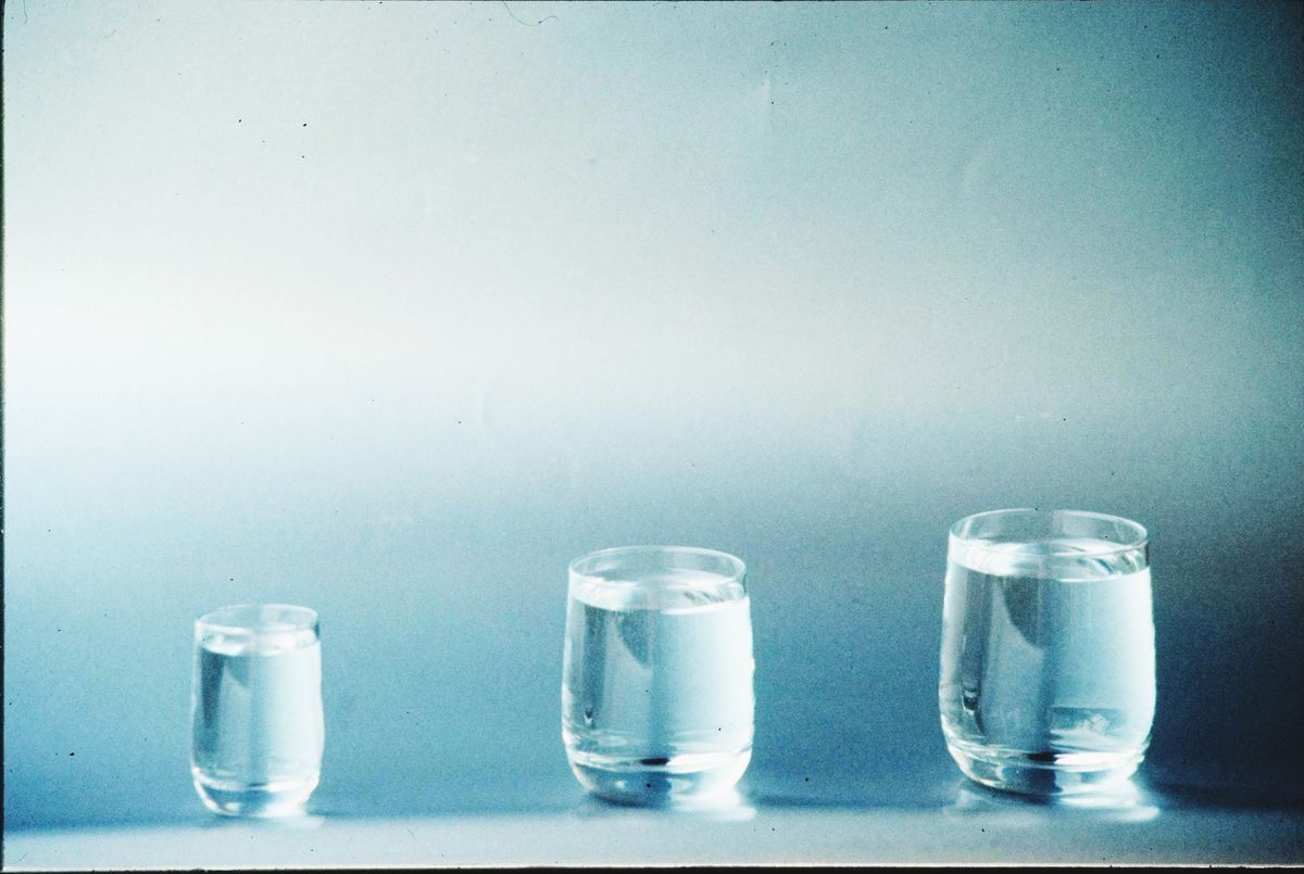 Three clear glasses of water of different sizes on a plain background, the setup for the settling test that identifies cloudy softened water
