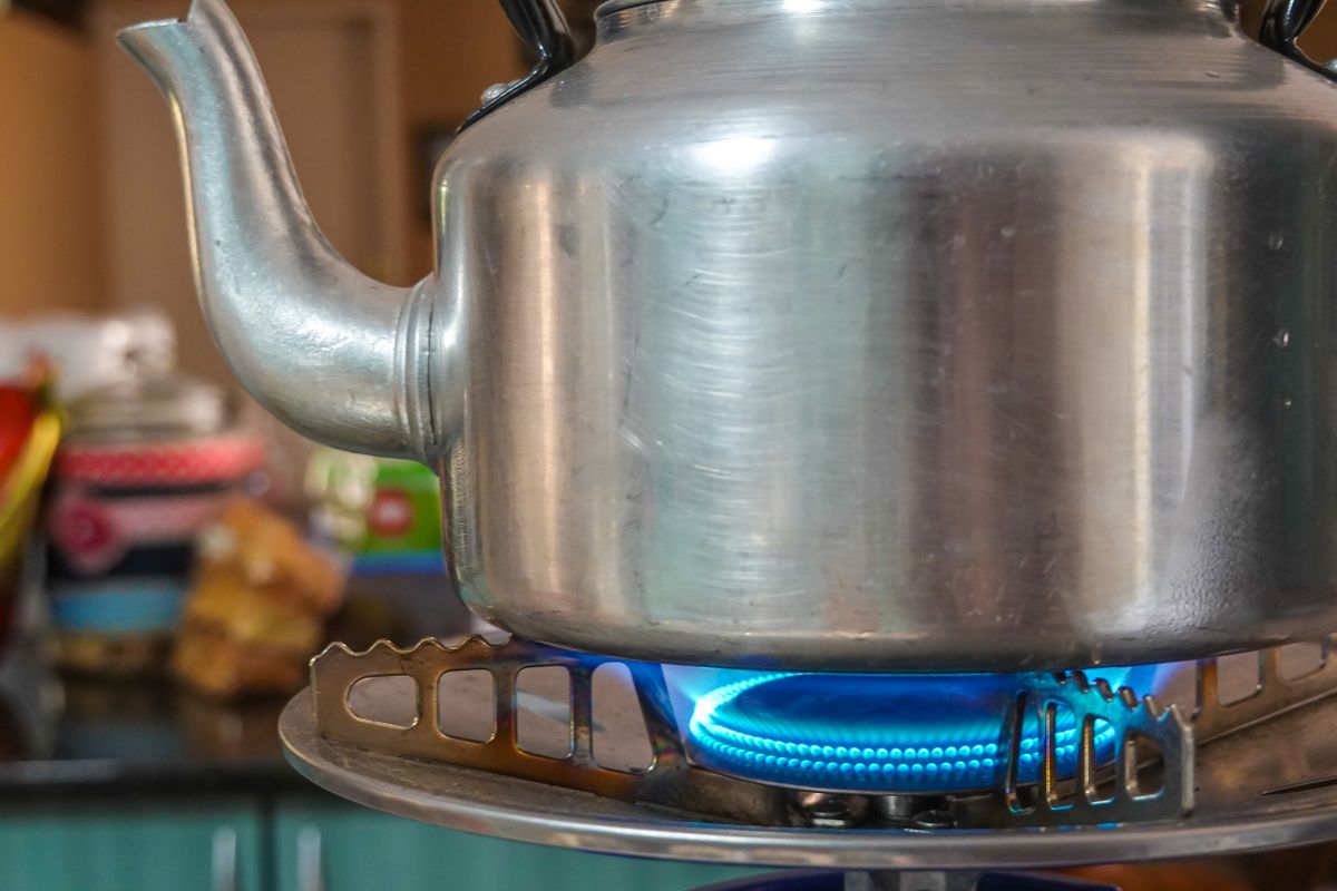 Stainless steel kettle heating on a blue gas stove flame