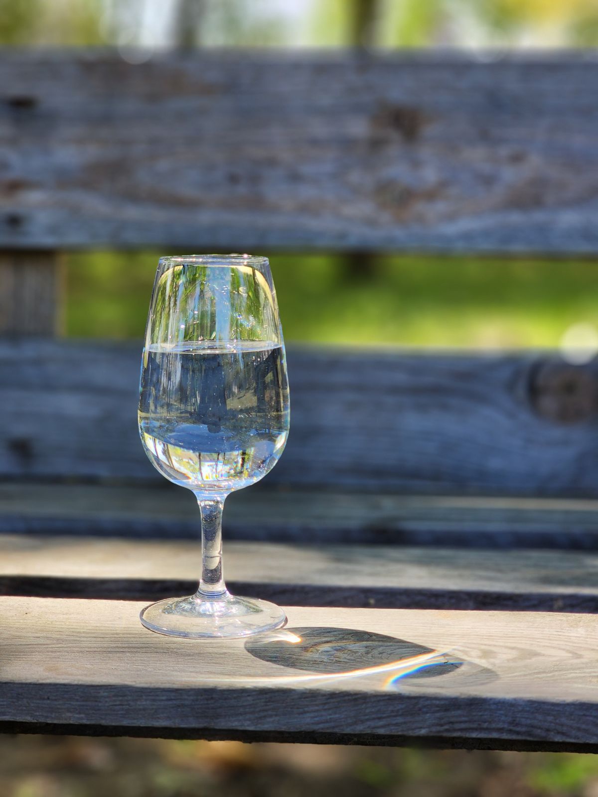 Clear glass of water on a weathered wooden bench, the kind of simple sample used to judge whether rinse water and the first softened water after a regeneration run clear