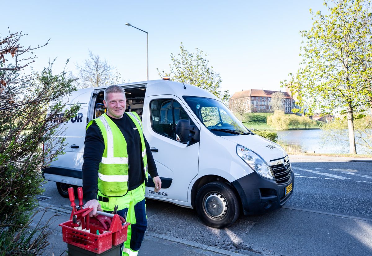 Service technician in a high-visibility vest standing beside a white work van with a crate of tools, the local dealer visit that comes with every Culligan water softener