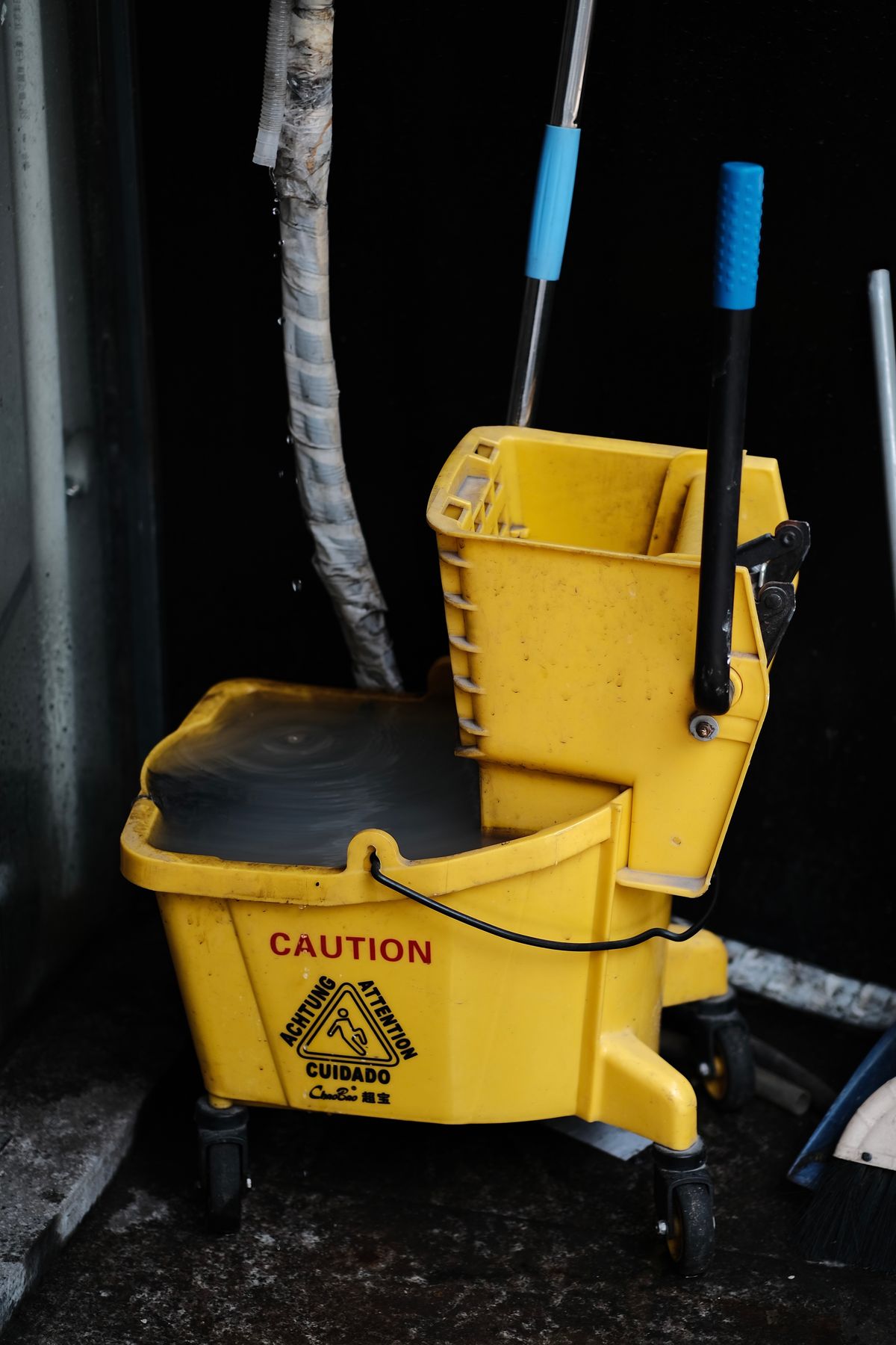 Yellow mop bucket holding dirty water with a caution sign beside it, the wet-vacuum-and-bucket stage of clearing sludge from a brine tank
