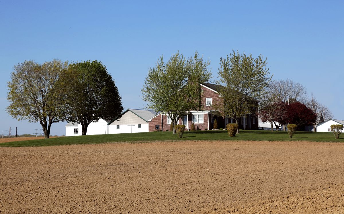Brick farmhouse and outbuildings behind a ploughed field, a rural private-well home where a dealer-designed softener and iron filter train can beat a cabinet unit