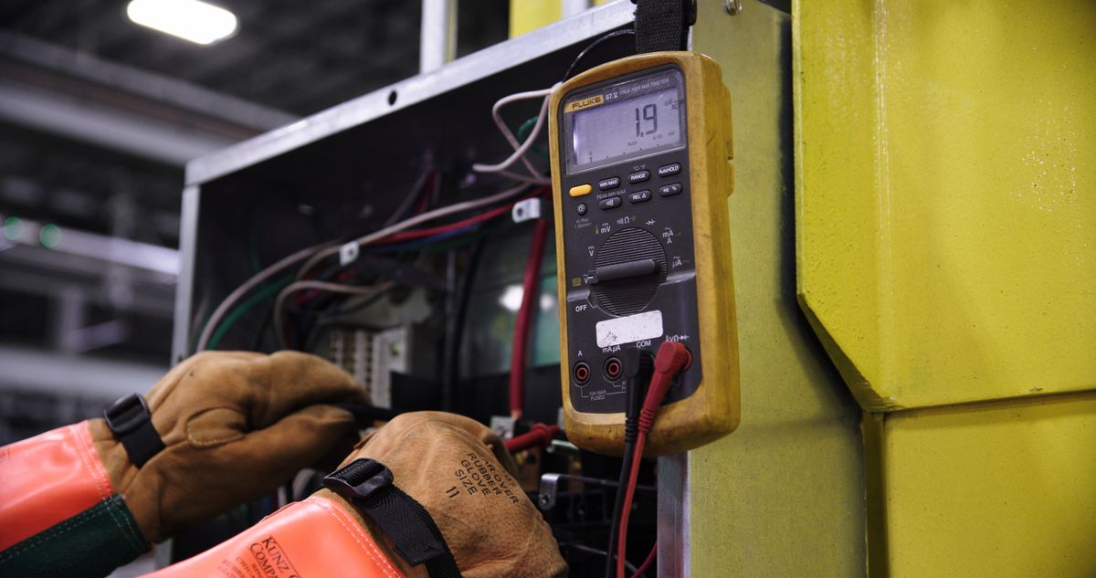 Gloved hands testing control panel wiring with a yellow digital multimeter, the kind of electrical check that comes late in the sequence when a softener will not regenerate