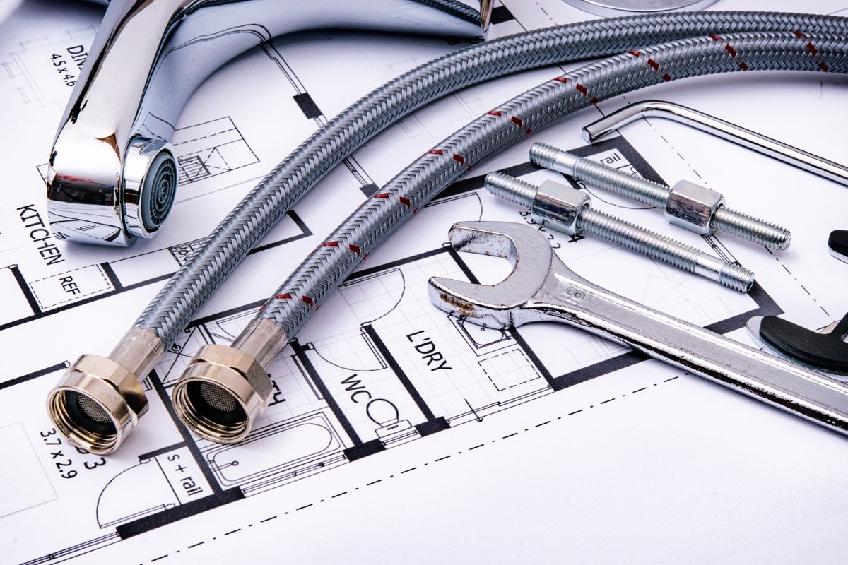 Plumbing tools and a faucet laid out on an architectural plumbing drawing, the kind of layout used to check flow direction and fittings after a softener install