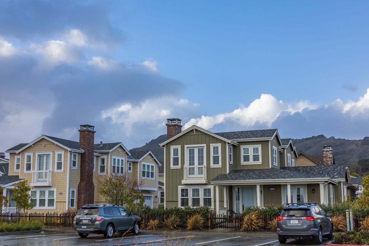 Row of modern two-storey suburban houses on a city street with parked cars, the typical municipal-water home choosing between a Culligan and a Whirlpool water softener