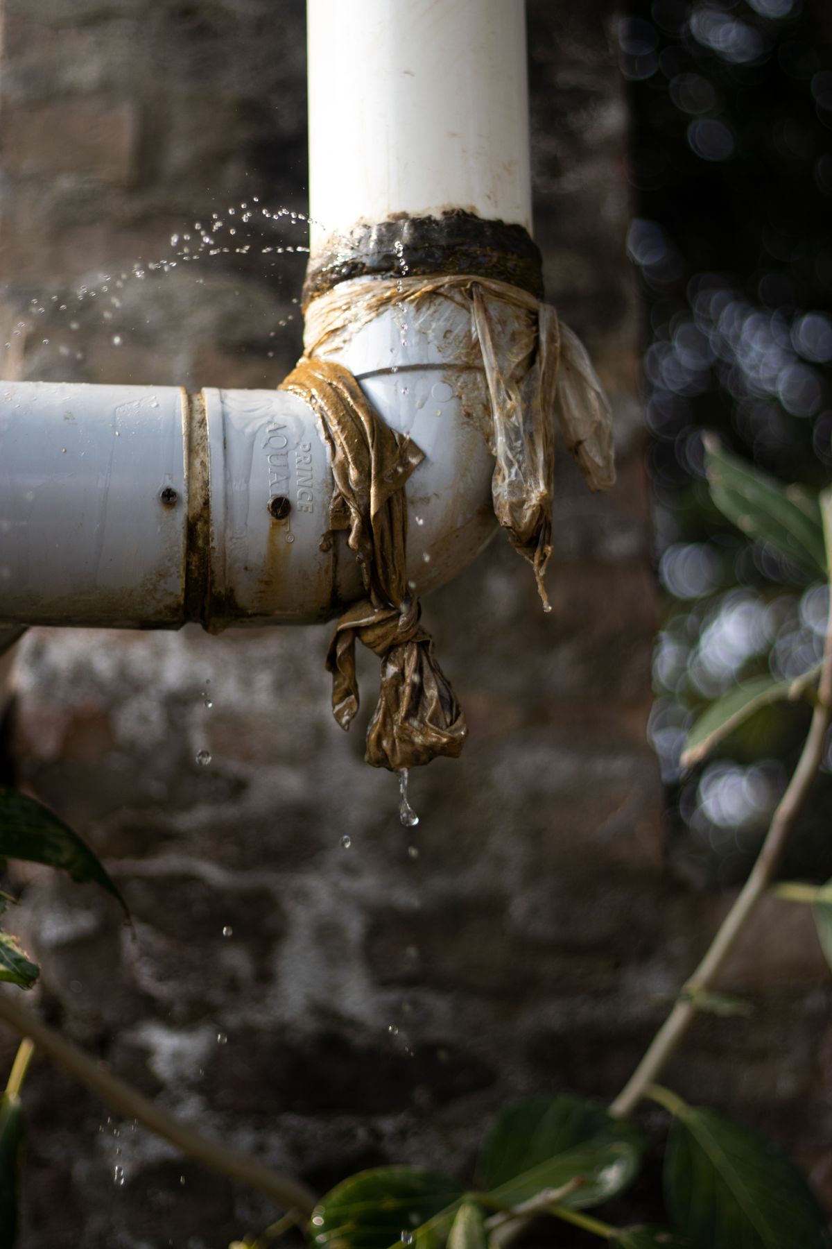 Close-up of a leaking plastic pipe with water dripping from a worn joint, the kind of slow seep that an external softener inspection is meant to catch