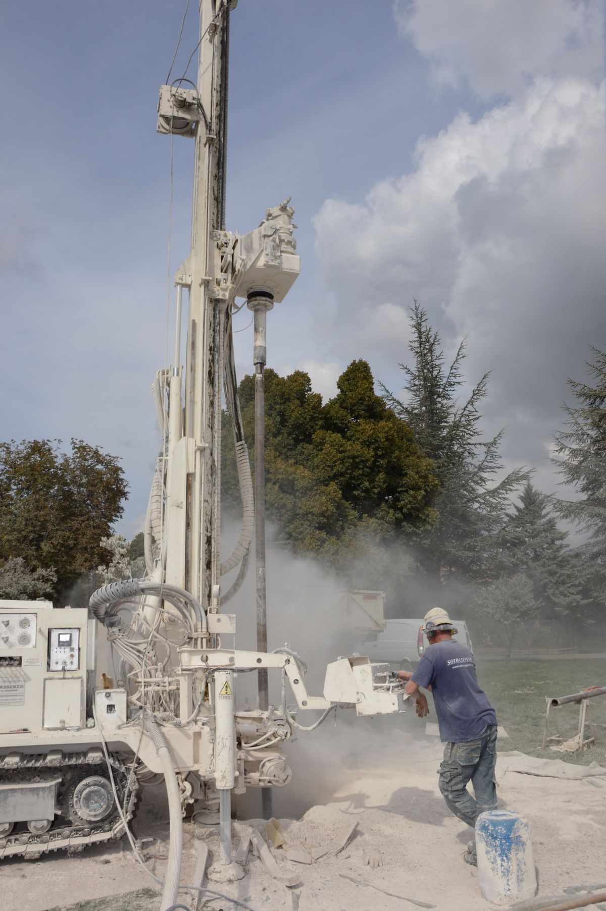 Drilling rig boring into the ground beside a field while a worker operates the controls; new drilling near an existing well is a common trigger for a change in its water supply