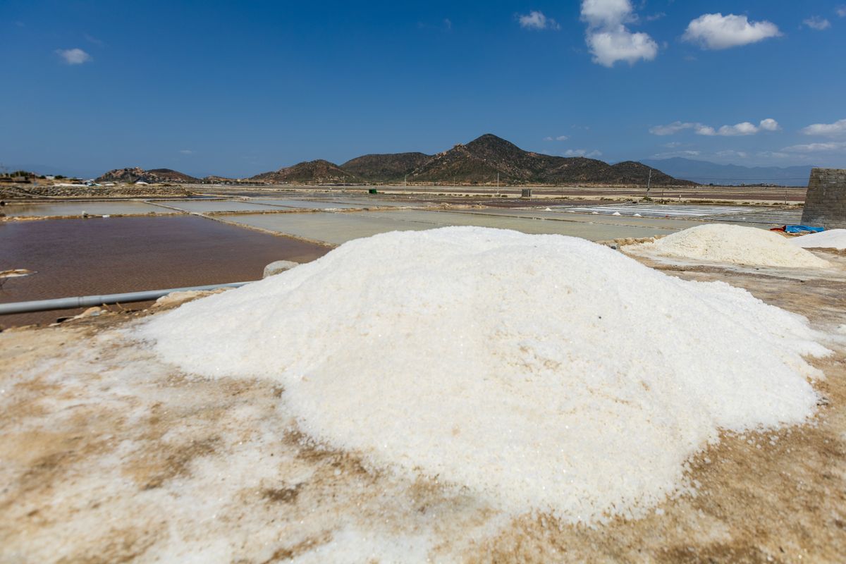 Large heap of white sea salt drying beside evaporation ponds at an outdoor salt works, the first stage of a softener's salt supply