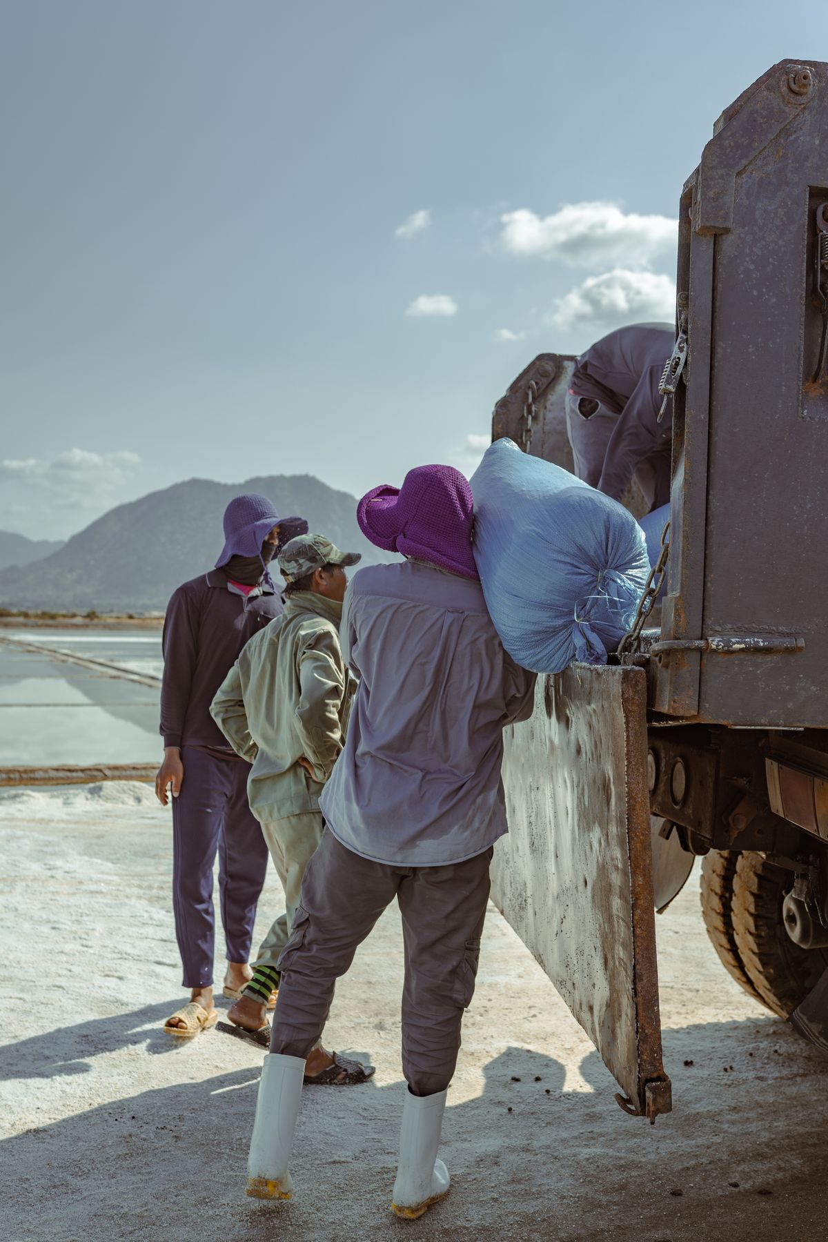 Workers loading bags of harvested salt onto a truck beside coastal salt fields