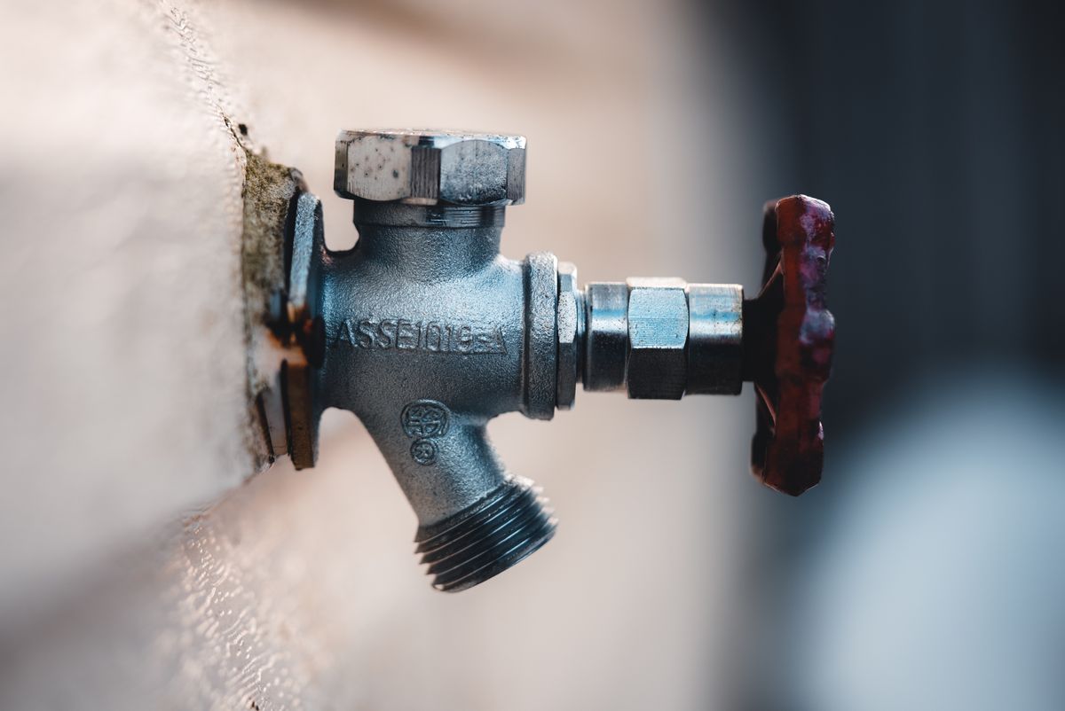 Outdoor hose bib faucet mounted on an exterior house wall where a pressure gauge attaches