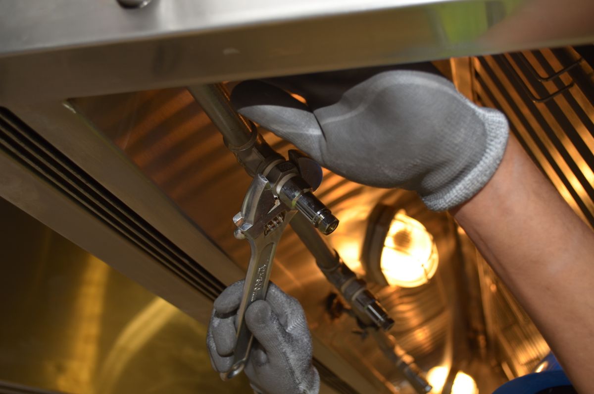 Worker using a spanner on pipework at close range, the drain line and flow control work that restores correct backwash to a softener