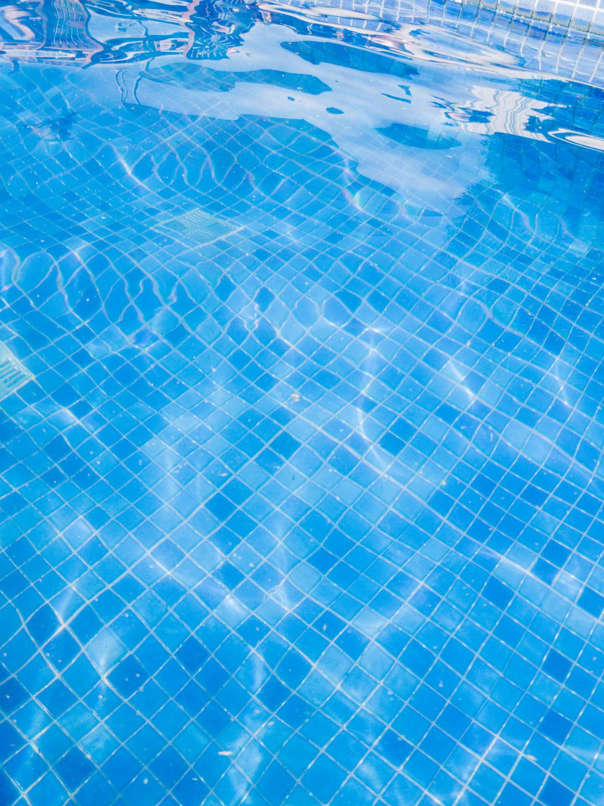 Blue tiled swimming pool floor seen through clear water, where grout lines are exposed to aggressive low-calcium water