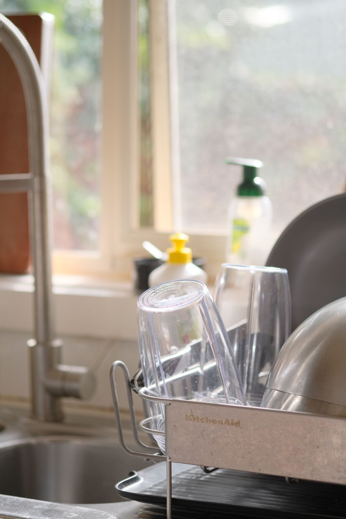 Drinking glasses draining in a rack beside a kitchen sink, where white spots remain after a water softener are first noticed
