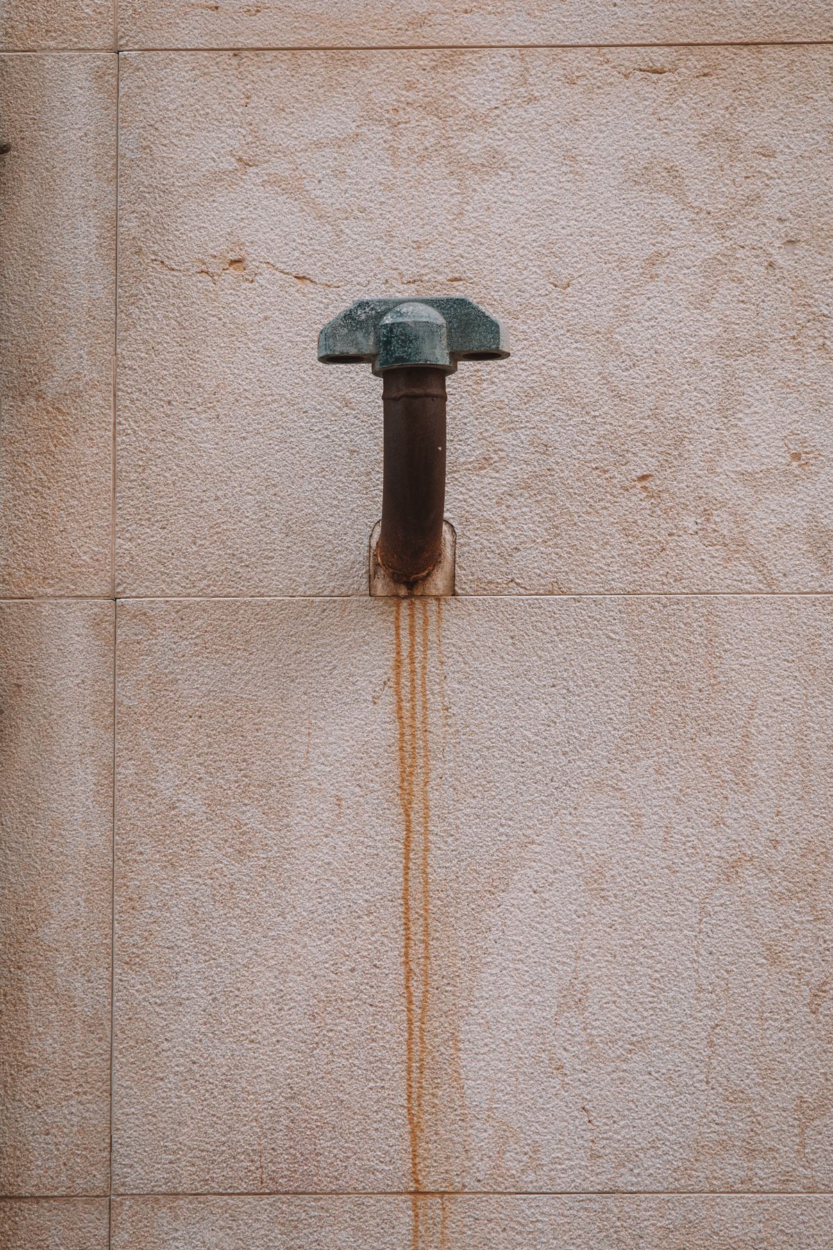 Corroded metal water pipe against a weathered wall, showing the iron staining that accompanies a fouled water softener resin bed