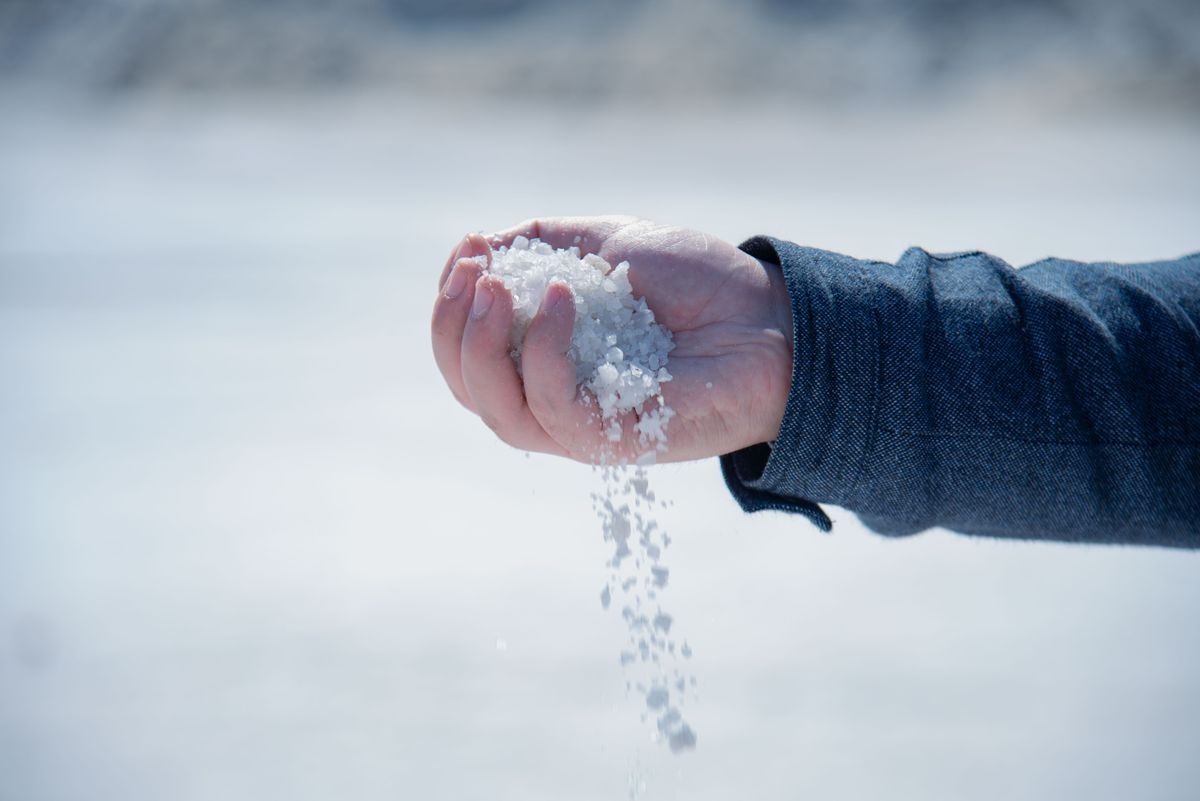 Close-up of a hand pouring coarse white salt crystals, the loose salt condition a brine tank should have all the way down to the water line