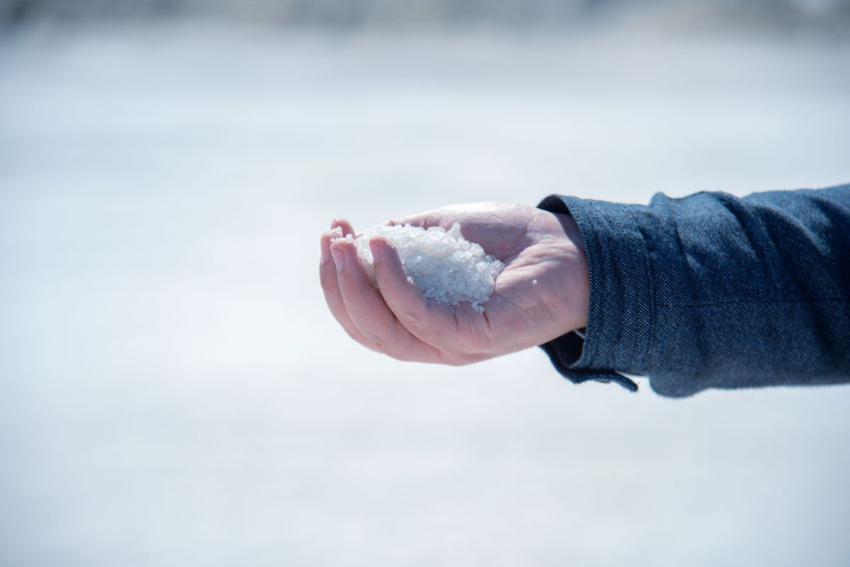A hand holding a small heap of white salt crystals outdoors, representing the fixed salt dose a softener is programmed to use in every regeneration