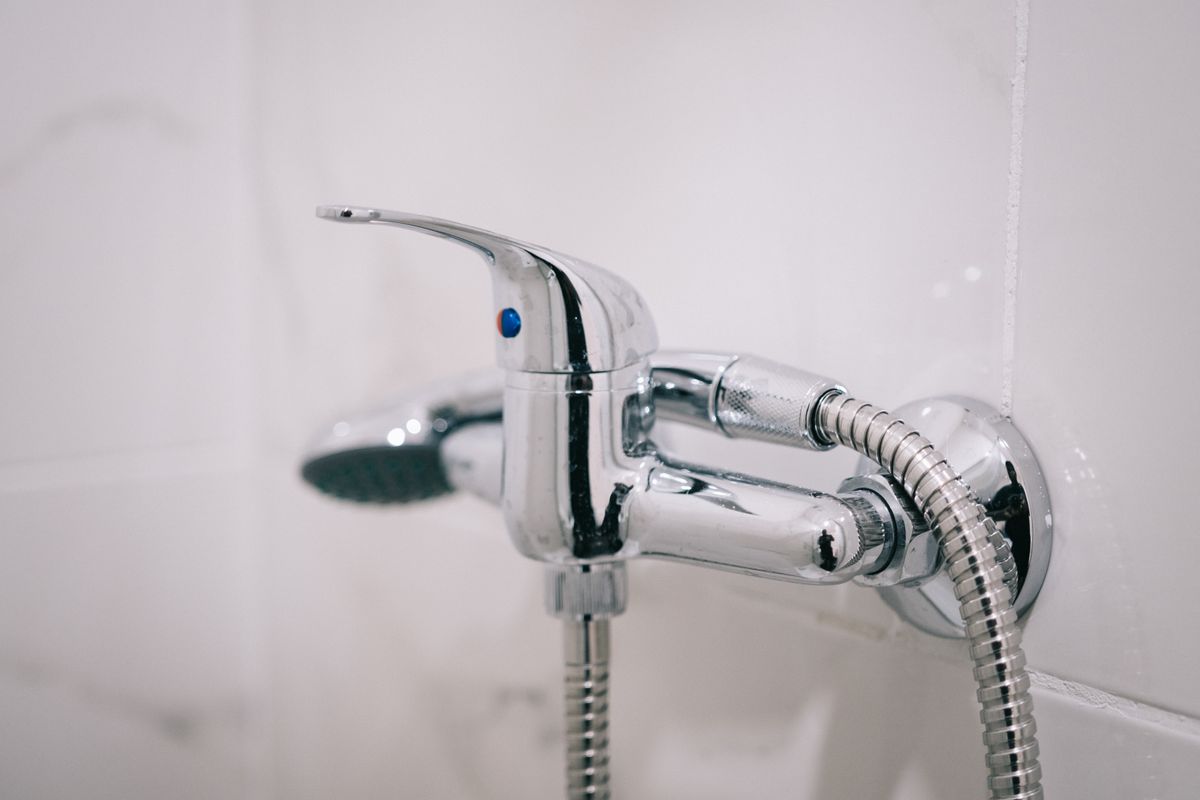 Chrome shower mixer and hose on a white tiled wall, a cold-water fixture where an electronic descaler such as the Eddy or ScaleBlaster does not stop hard water spotting