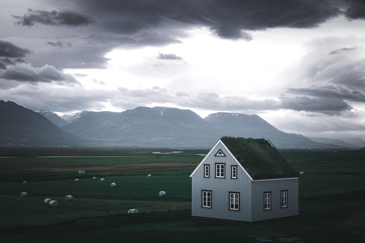 Isolated farmhouse with a turf roof on open grassland below mountains, far from any water main, so the house relies on a private well