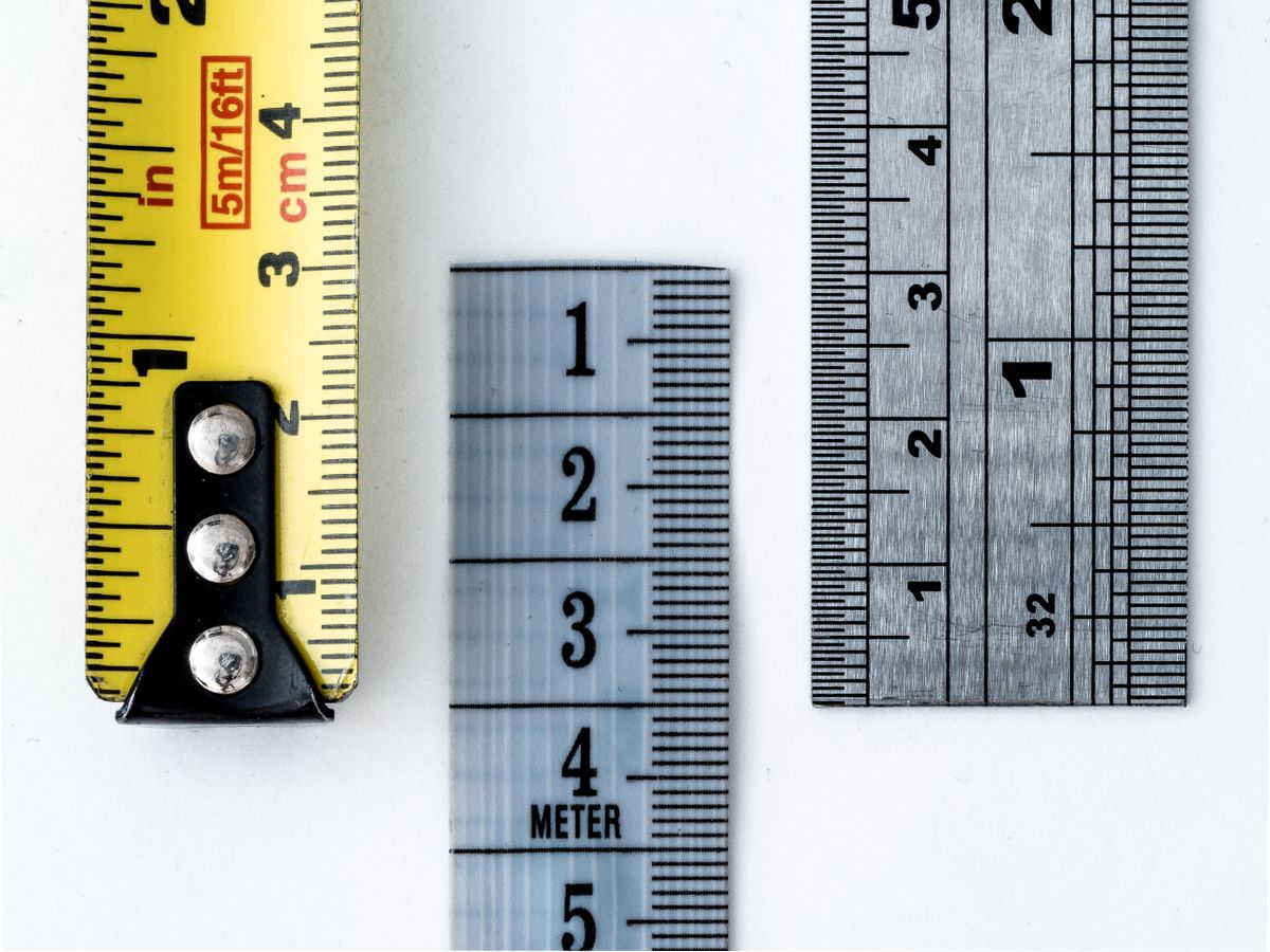 Measuring tapes and rulers laid out showing millimetre, centimetre and inch markings, the measurement discipline that a brine tank salt level actually requires
