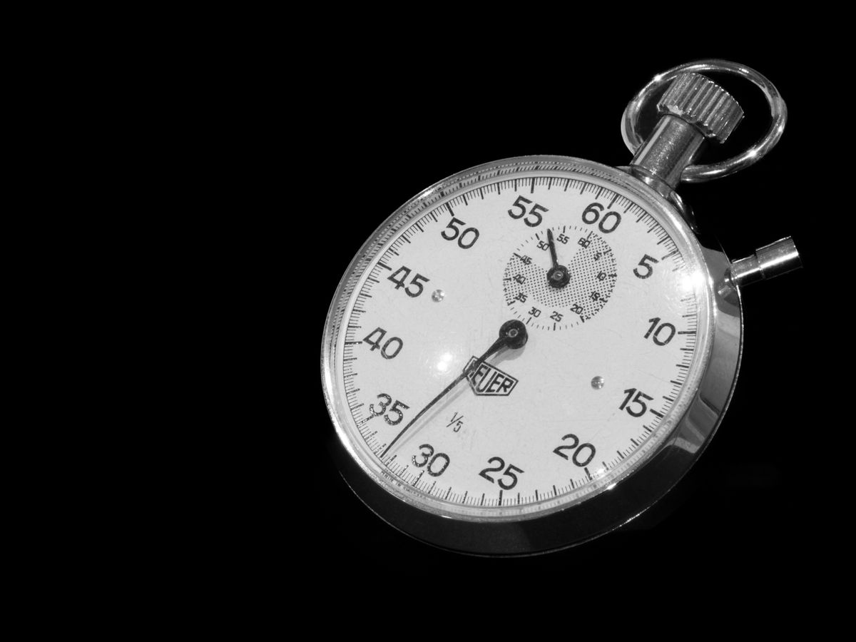 Silver mechanical stopwatch on a black background, the kind of timer used to track each stage of a manual softener regeneration against the valve's programmed step times