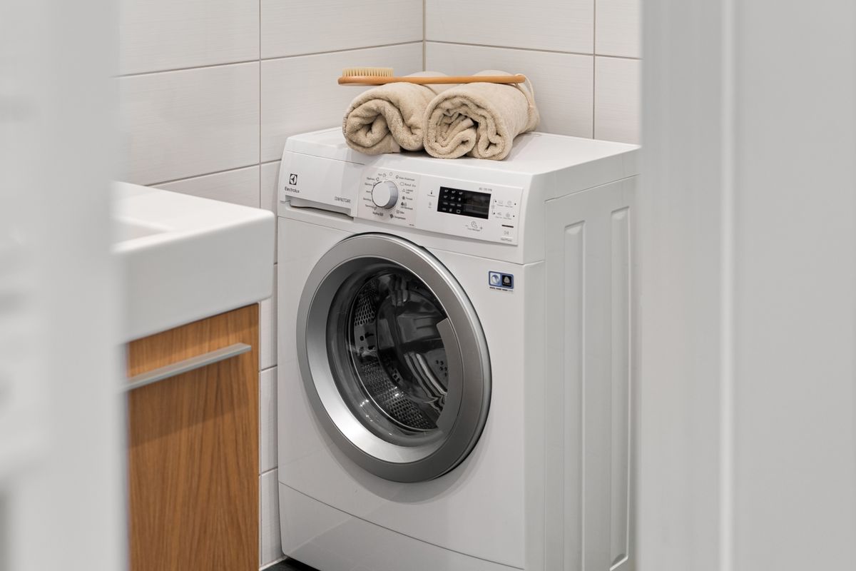 Front-loading washing machine with rolled towels on top in a tiled bathroom, one of the heavy water uses that outruns an undersized water softener