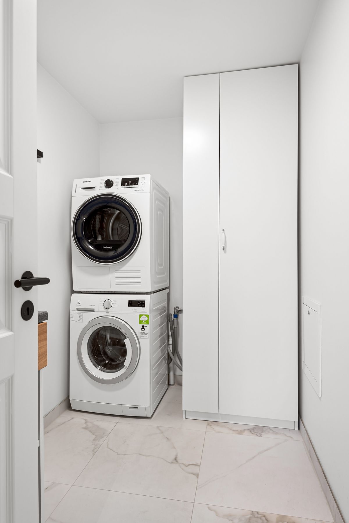 Compact laundry room with a stacked washer and dryer beside tall white cabinets, a utility space where an EcoPure cabinet water softener could stand
