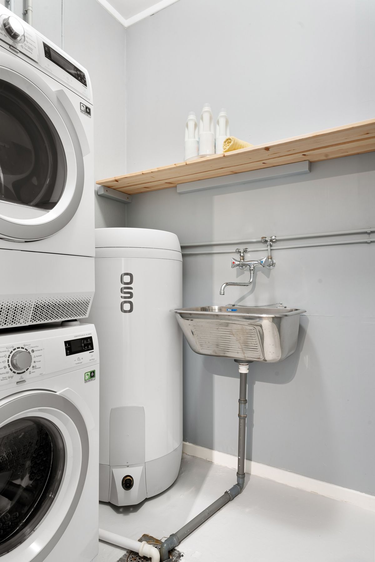 Utility room with a stacked washer and dryer, a water heater and a steel utility sink draining into the house wastewater pipe